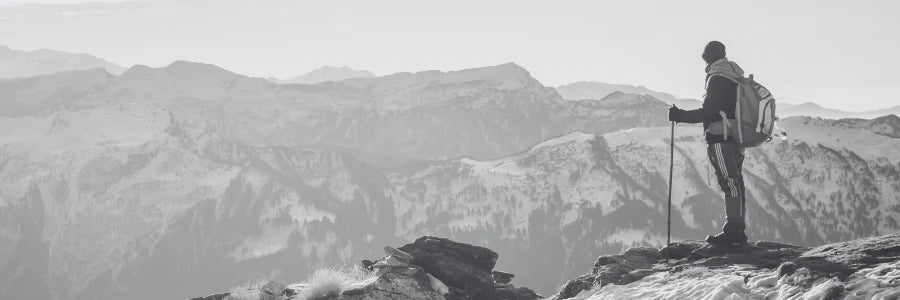 The image shows a hiker on a snowy mountain summit, gazing into the distance, representing Covert Threads' ability to make tough socks for extreme cold conditions.