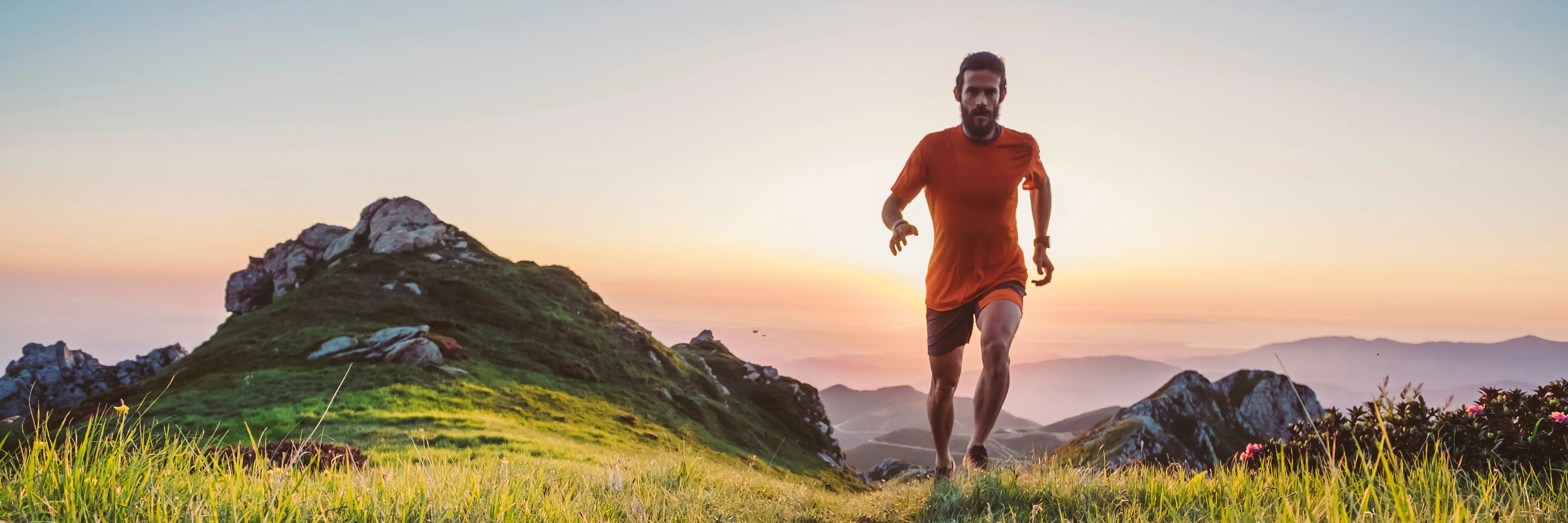 The image shows a man trail running up a mountain ridge at sunrise, demonstrating Covert Threads' ability to make athletic performance socks for hard training in any terrain
