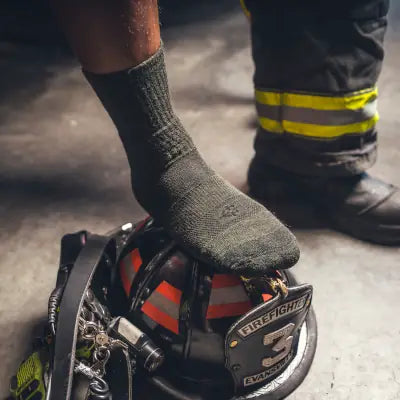 Covert Threads work socks worn by a firefighter, foot resting on a fire helmet