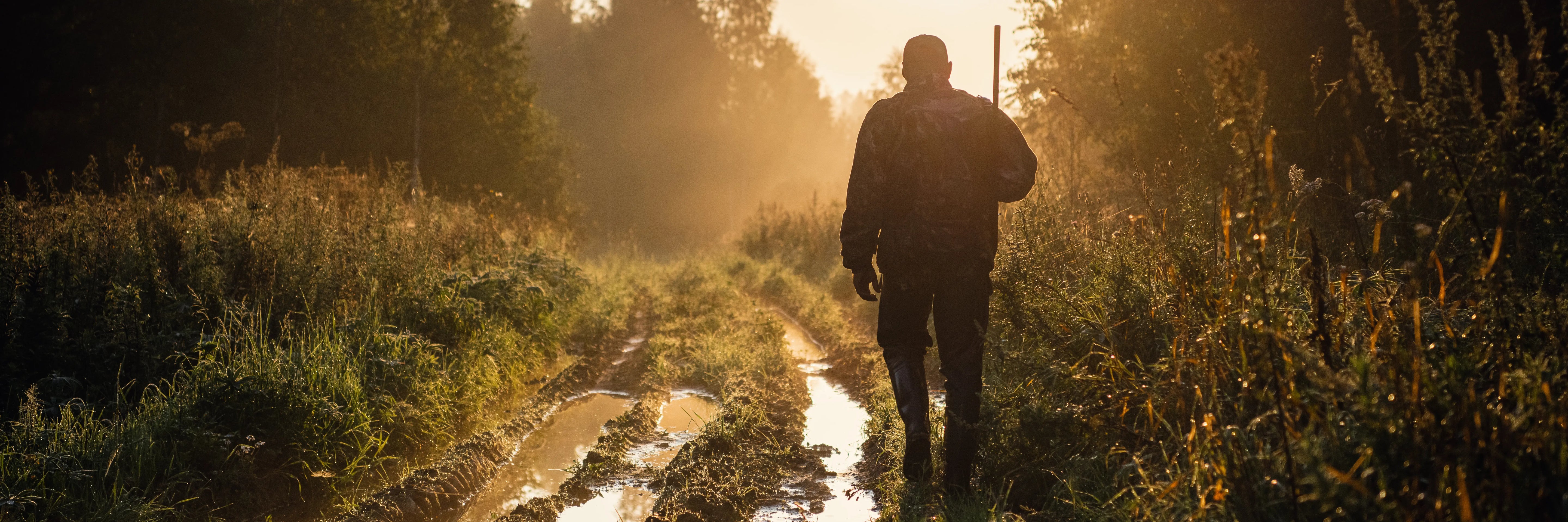 The image shows a many hiking along a muddy road on his way to a hunt, representing Covert Threads' ability to make socks suitable as hunting socks, hiking socks, or as socks for any other outdoor activities. 