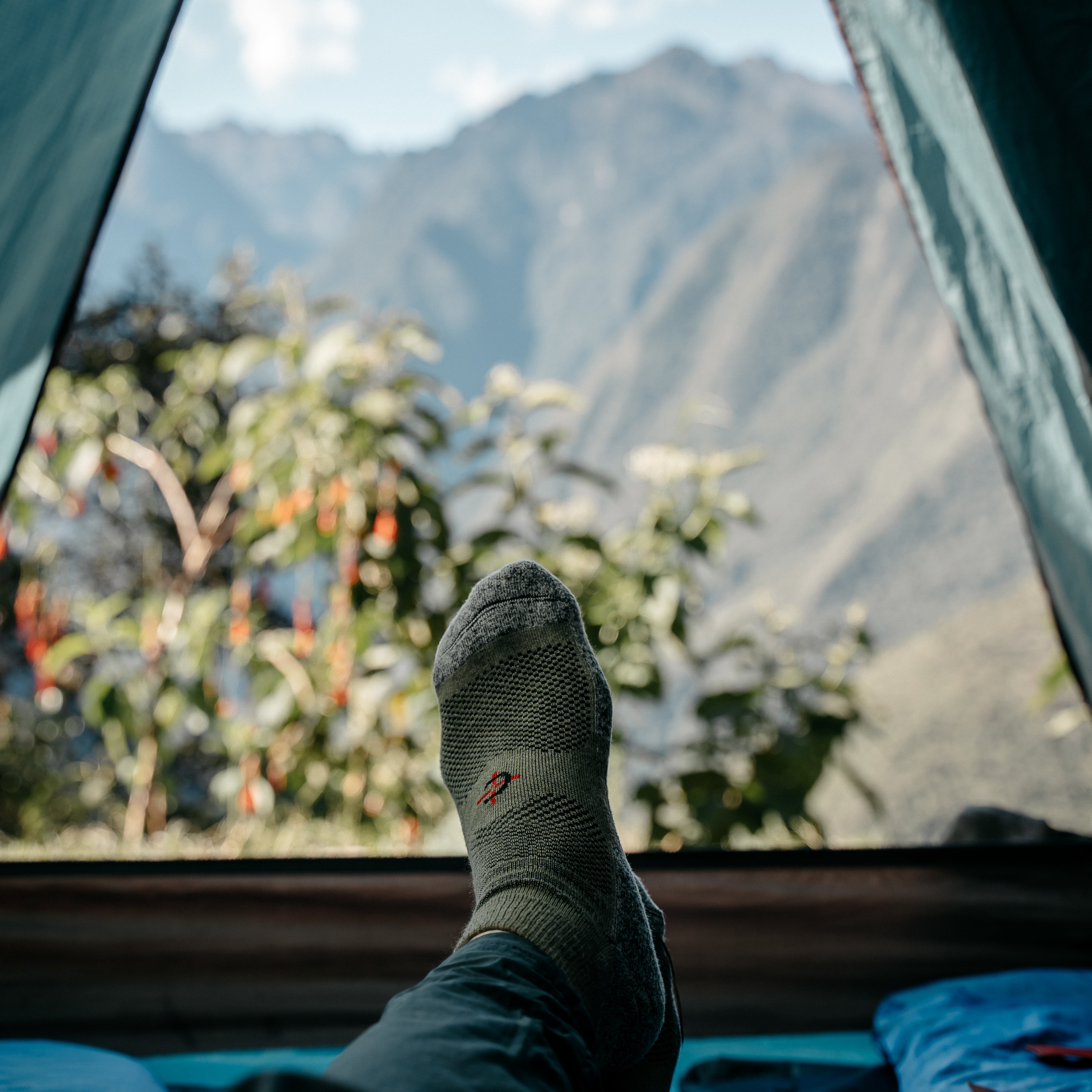 Covert Threads outdoor socks worn resting in a tent, mountains framed in the doorway