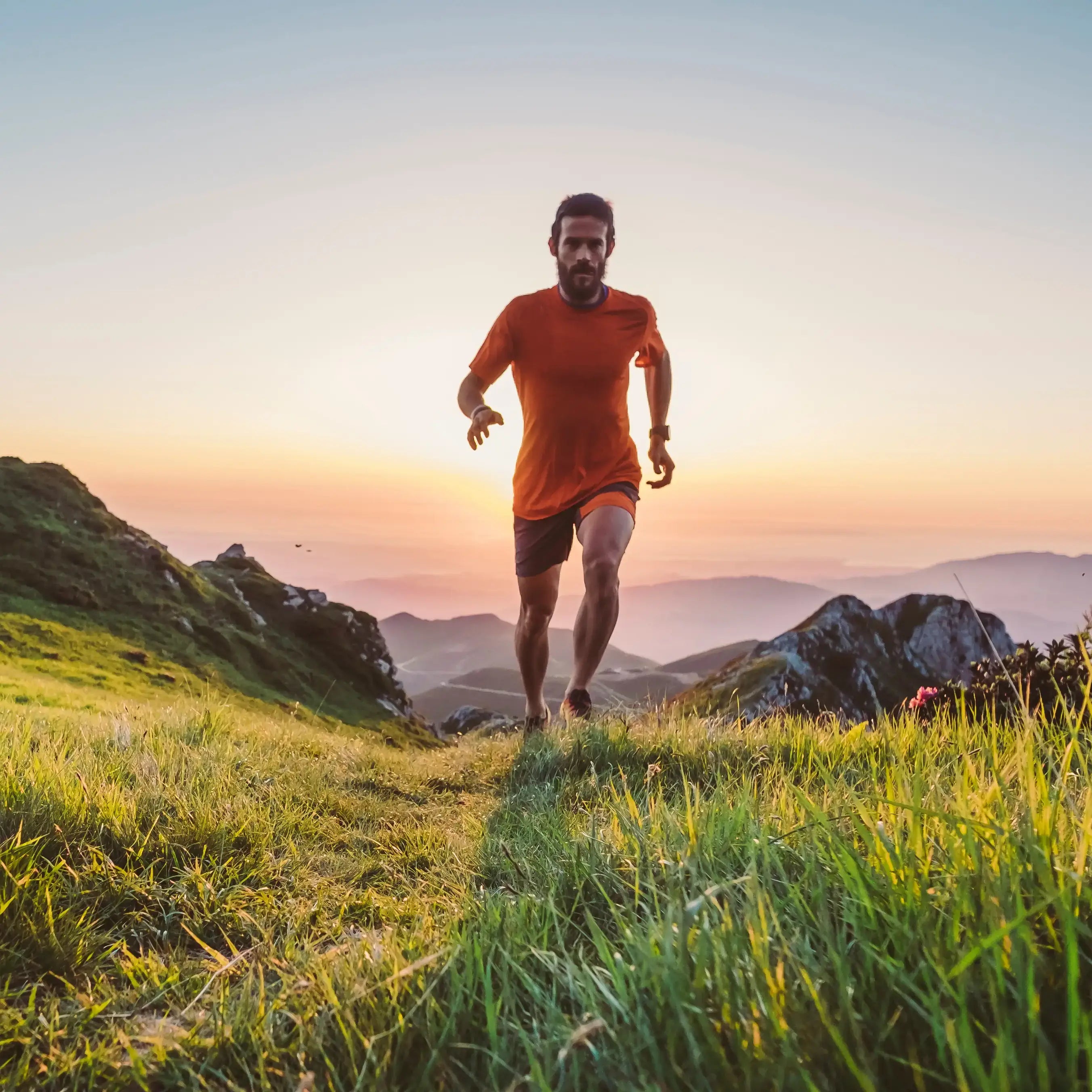 A trail runner ascending a grassy ridge at sunrise, symbolizing the activities that can be performed wearing Covert Threads athletic socks